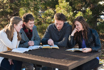 college students sitting at a picnic table reading from Bibles during a Bible study