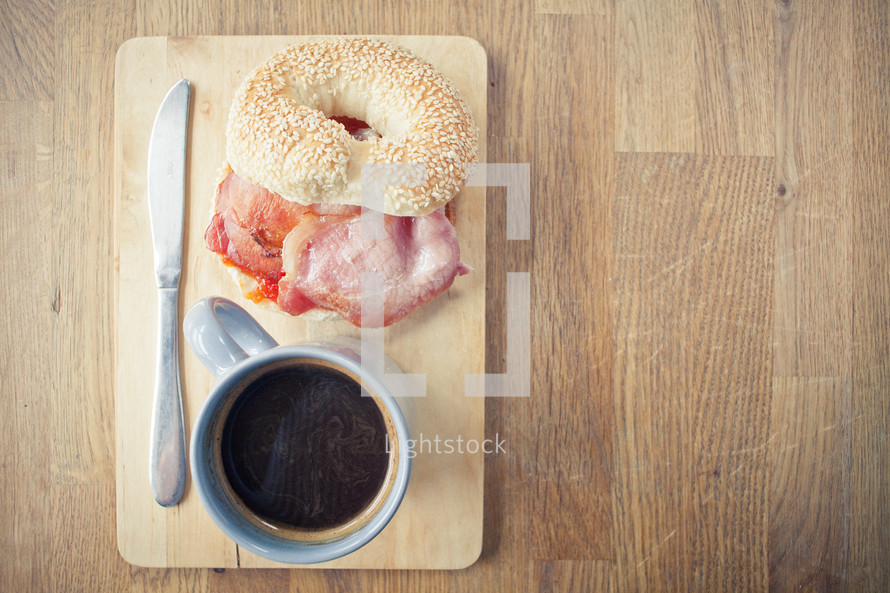 bacon, bagel, coffee, and knife on a wood plate 