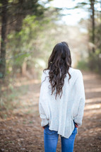 woman in a sweater walking on a path in a forest 