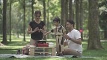 Portrait of Small and Happy Asian Family Enjoying Activities at The Park - Picnic and Cooking - Father, Mother and Child in Slow Motion