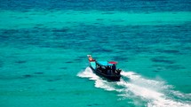 Wooden boat in turquoise sea, movement on blue water. Trip boat with tourists sailing on clean blue sea surface. A long-tailed Thai boat sails among the islands, touristic excursion ride. Aerial. 