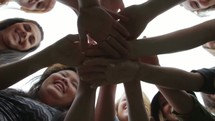 Shot from beneath - a group of friends putting their hands together as in a huddle, then pans down the line of the people holding hands