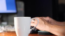 A man sets down a cup of coffee and works at his computer