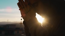 Man prays at sunset with rosary