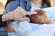 An elderly person's hand touching the top of an infant's head.