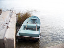A light blue colored row boat with two oars sits parked beside a concrete pier off the ocean near Saint Augustine, Florida awaiting a fishermen to go out fishing. 