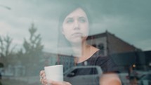  woman holding a coffee cup and looking out a window 