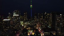 Aerial nighttime shot of vibrant downtown Toronto at night. Drone flying over the financial district with moderate traffic congestion. Slow camera movement to the right side. Illuminated cityscape.
