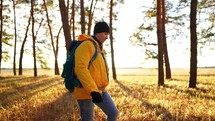 Adventure concept. A young man hiking a pine autumn forest, the sun rays in the background. Male tourist with backpack walking in wild pine forest. Active travel lifestyle. Amazing sunset.