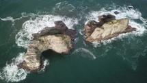 aerial view over waves crashing into rocks in the sea 