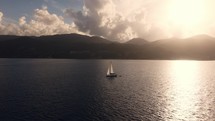 Yacht sailing during a scenic sunset at the coast of Zakynthos, Greece, aerial view with mountains and clouds in the background
