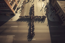 People gathering in the shape of a Cross in the middle of a street