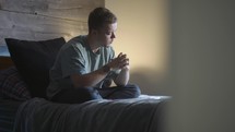 a young man sitting in bed praying 