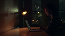 a woman looking at the internet at night in a dark apartment 