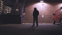a young man looking down at the ground standing in a parking lot at night 