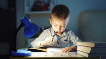 Children and education. Young boy Studying at desk in evening. Little boy writing on a notebook. Young caucasian male child is very concentrated doing his homework at desk in his room.