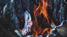Slow motion stationary clip of a camp fire with wood burning, ashes, and coals.