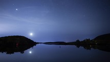 Timelapse of the moon and stars setting over a calm peaceful lake
