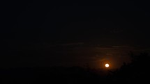 Timelapse of an orange moon rising through clouds