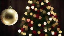 Gold ball decoration with blurred Christmas tree 