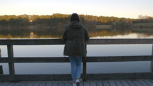 a woman looking over a railing at a lake 