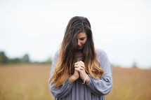a woman standing in a field with head bowed and praying hands 