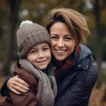 A happy mother and her son embrace outdoors on a cozy autumn day