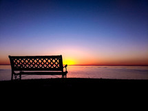 empty park bench with ocean view at sunset 