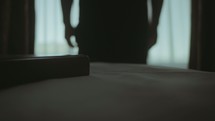Man standing in front of window, early in the morning and a bible on top of the bed. (Slow motion)