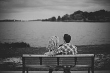 Couple sitting on a park bench by the ocean.