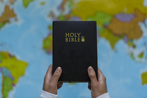 hands holding up a Bible in front of a map 