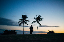 silhouette of a man standing between two palm trees 