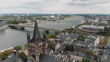 Flying over the historical Great Saint Martin Church towards the Deutz Suspension Bridge spanning over the Rhine River in Cologne, Germany.