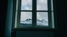 looking through a window at clouds moving over a mountain 