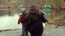 mother and son standing at the edge of a pond 