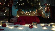 Child sleeping on the carpet under tree lights 