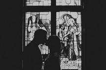 A silhouetted couple kissing in front of a stained glass window