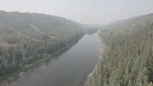 Drone shot of trees and a river in a canyon with a smokey atmosphere.