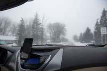 view of a snowy road through a car window and dashboard 