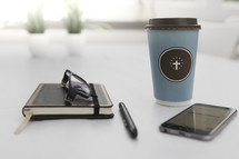 coffee mug, reading glasses, journal, cellphone, and pen 
