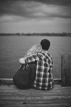 Embraced couple sitting on a wooden pier.