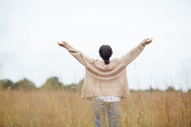 a woman standing in a field with outstretched arms 