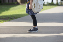 A little girl standing on a sidewalk wearing a backpack.