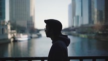 Silhouette of a young man standing on a bridge looking out towards the river, urban environment