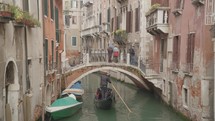 The atmosphere of narrow canals in the city of Venice, with many bridges and small boats parked.