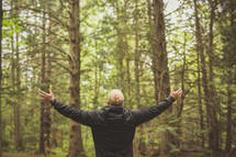 a man standing in a forest with outstretched arms 