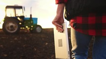 Silhouette woman walking across field to tractor with tablet in her hands to control production process in agricultural farm. Machine equipment for reducing work and increasing sales in agribusiness.