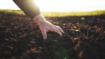 Farmer hand scooping dirt on a field at sunset. Man grabbing the soil dirt from the ground. Close up of male hands touching dry ground in an agricultural field. Concept of agribusiness.