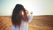 Young woman tourist in Dubai rear view from back stands in desert and stretches arms forward and sunbathes under sunlight enjoying warm weather. Traveling on vacation to beautiful places of world.