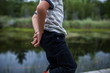 a boy standing in front of a pond 